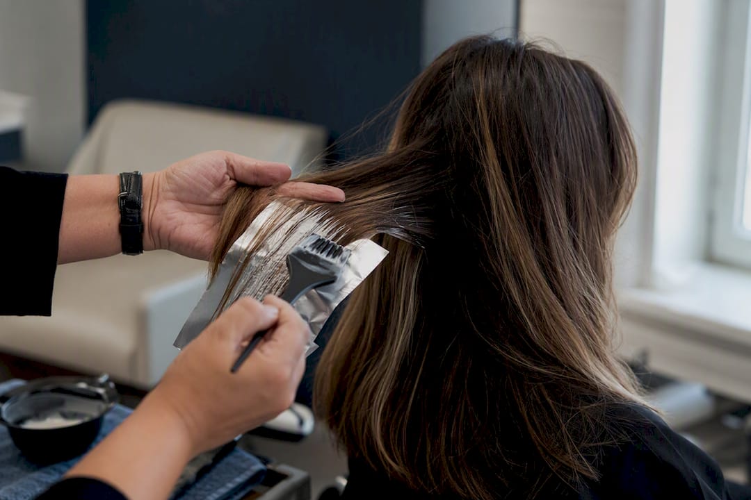 Hands painting balayage highlights on hair mid-lengths