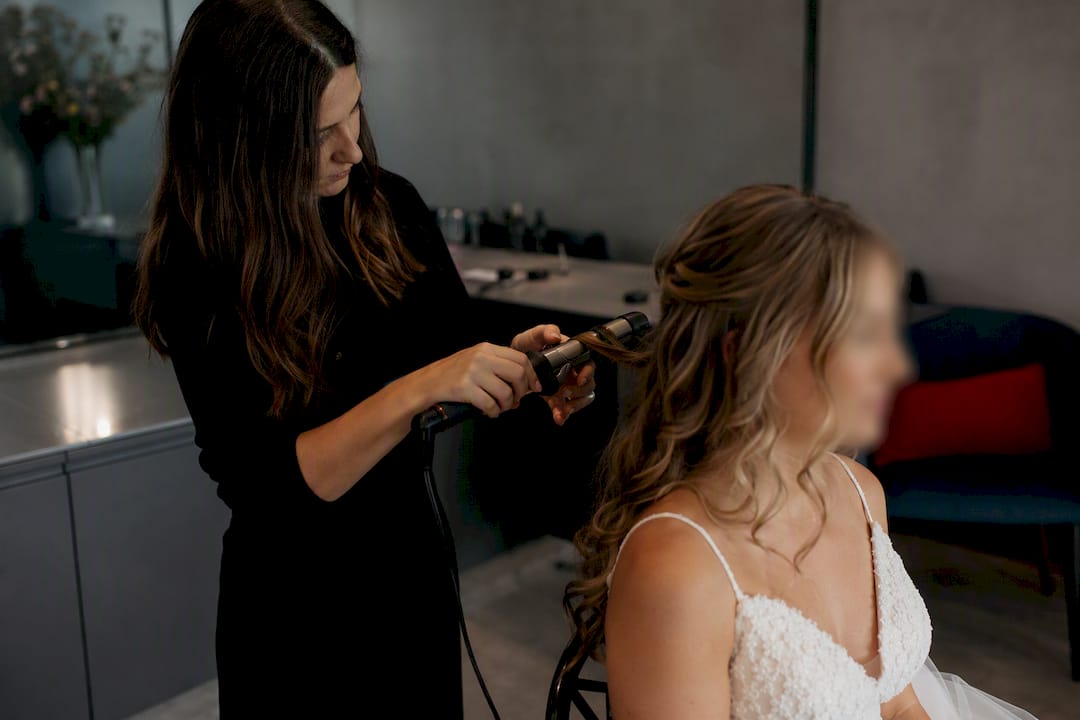 Stylist finishing hot-tool styling before makeup on bride