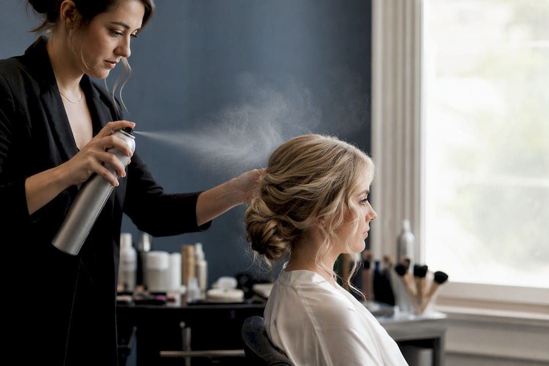 Stylist spraying bride’s styled hair before makeup