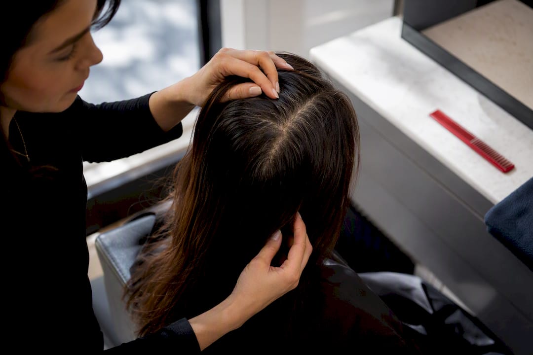 Colourist inspecting visible hair root regrowth