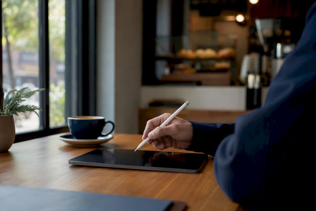 Hand with stylus above blank tablet by coffee cup