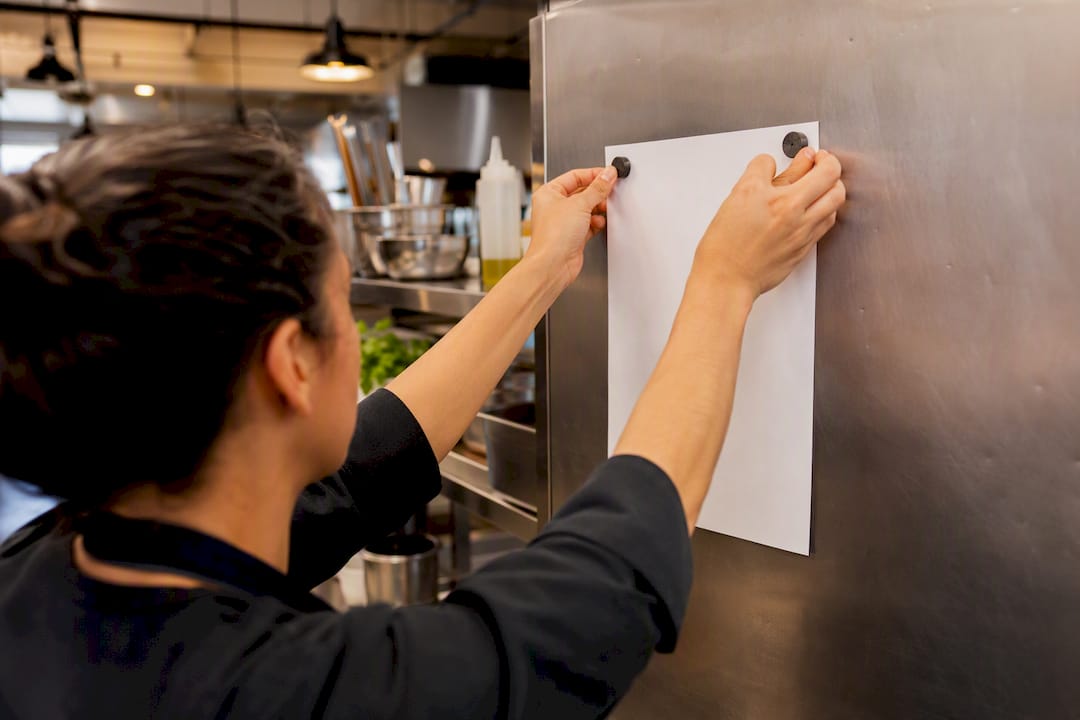 Hand pinning roster sheet on kitchen board