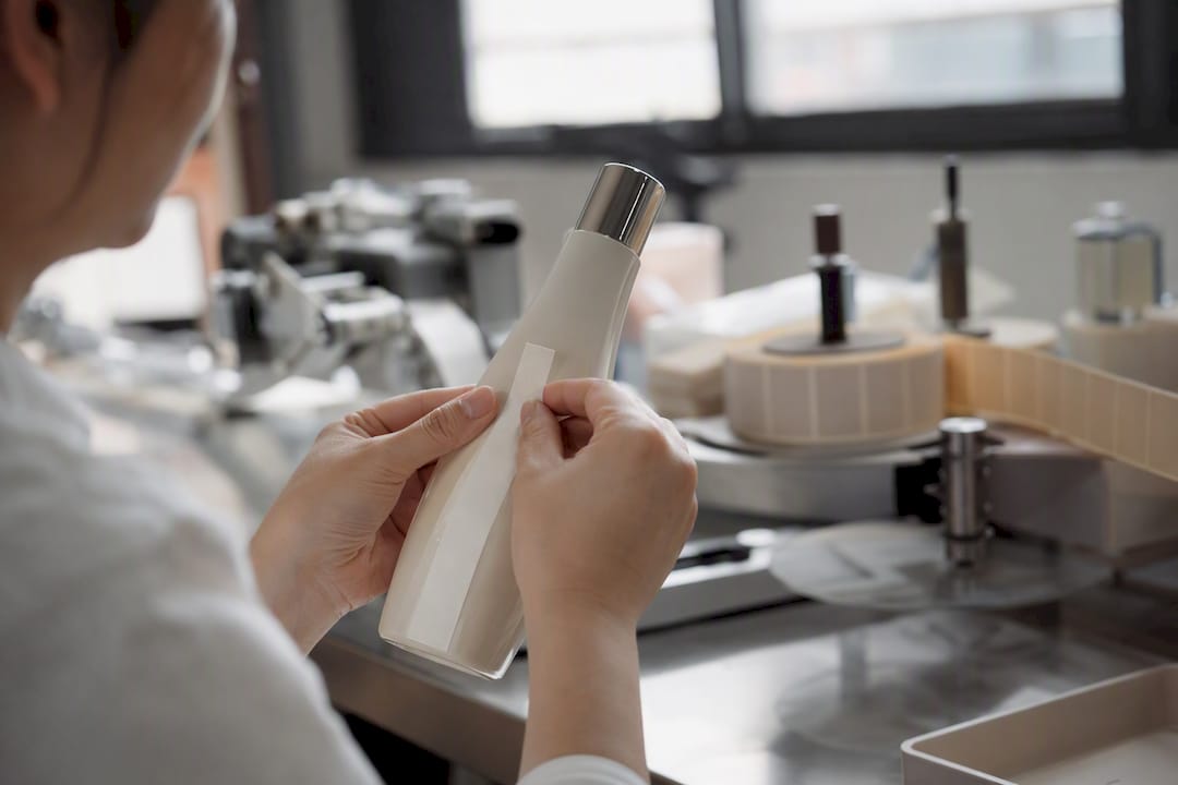 Hands applying pressure sensitive label on bottle