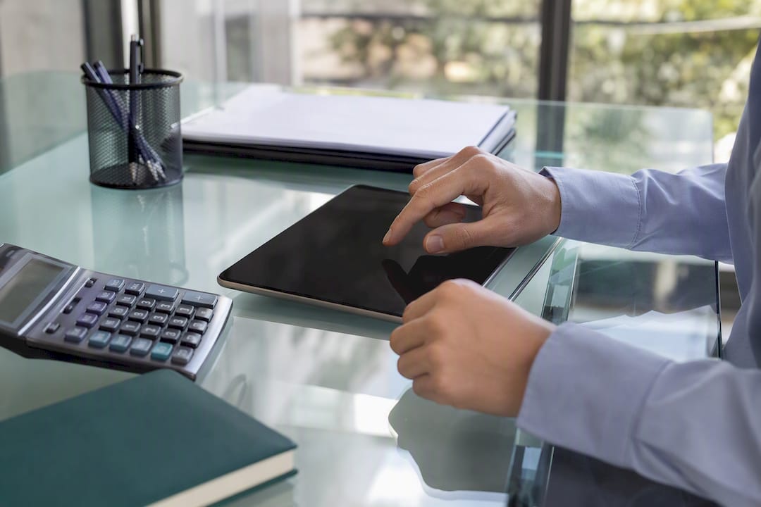 Hands hovering over tablet with magnifying glass and calculator