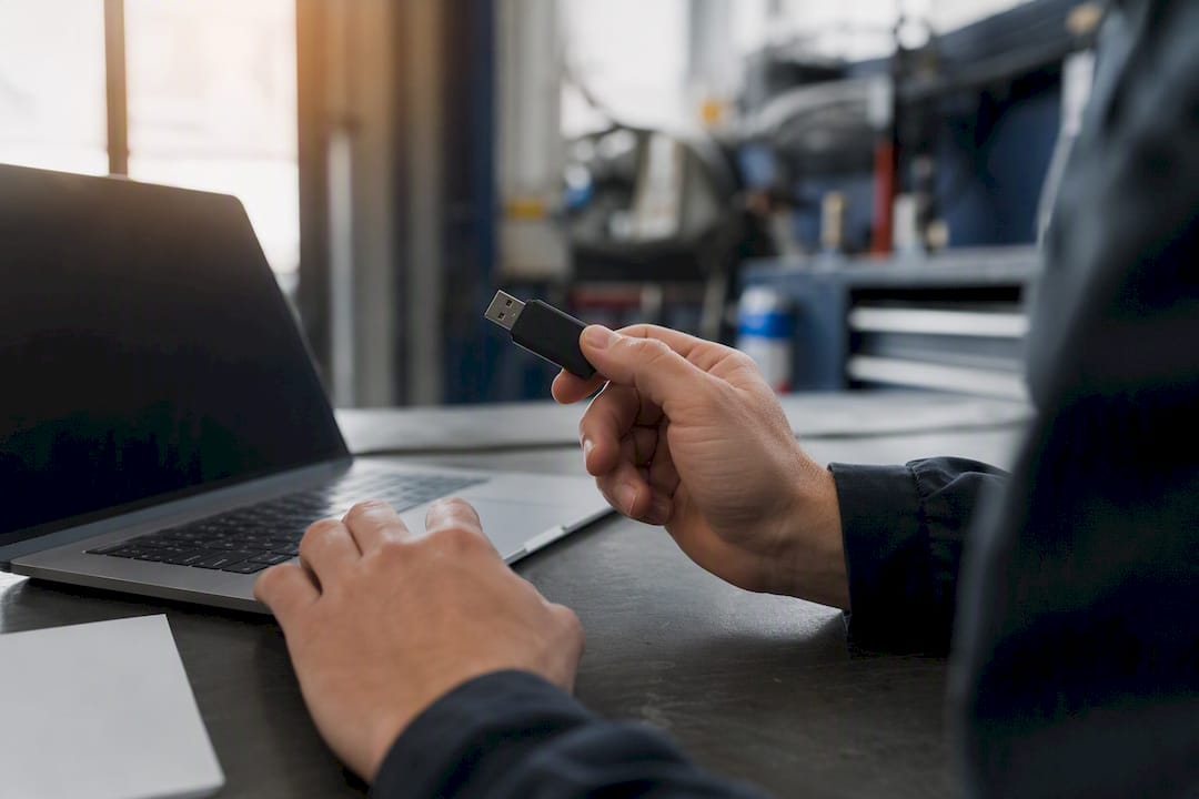 Hände halten USB-Stick neben Laptop