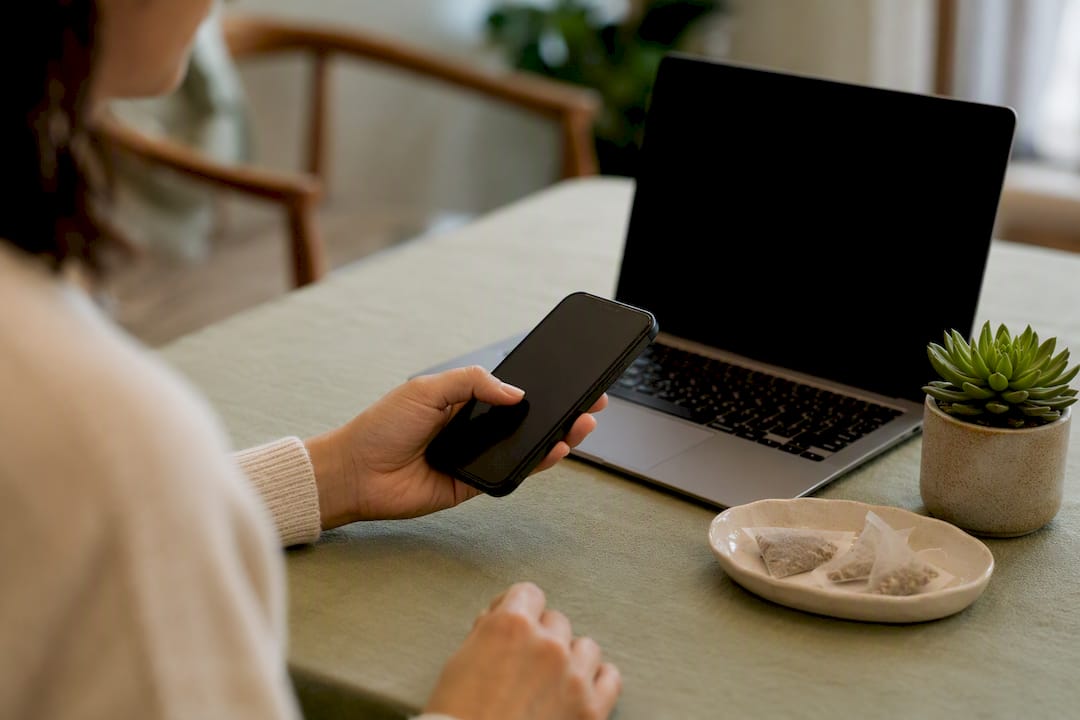 Hand holding smartphone near laptop on desk