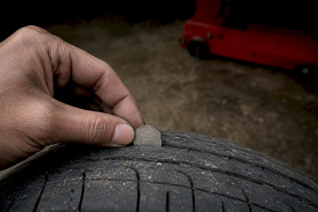 Hand measuring car tyre tread with coin