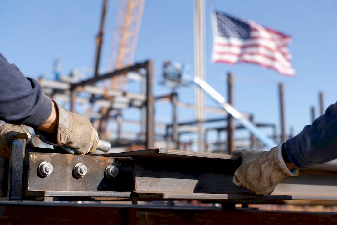 Arbeiterhände montieren Stahlträger vor US-Flagge