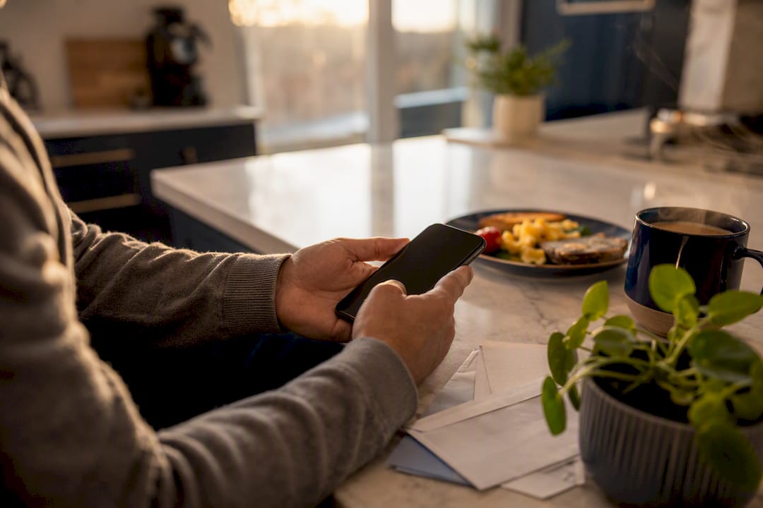 Hands holding a smartphone with bills on table