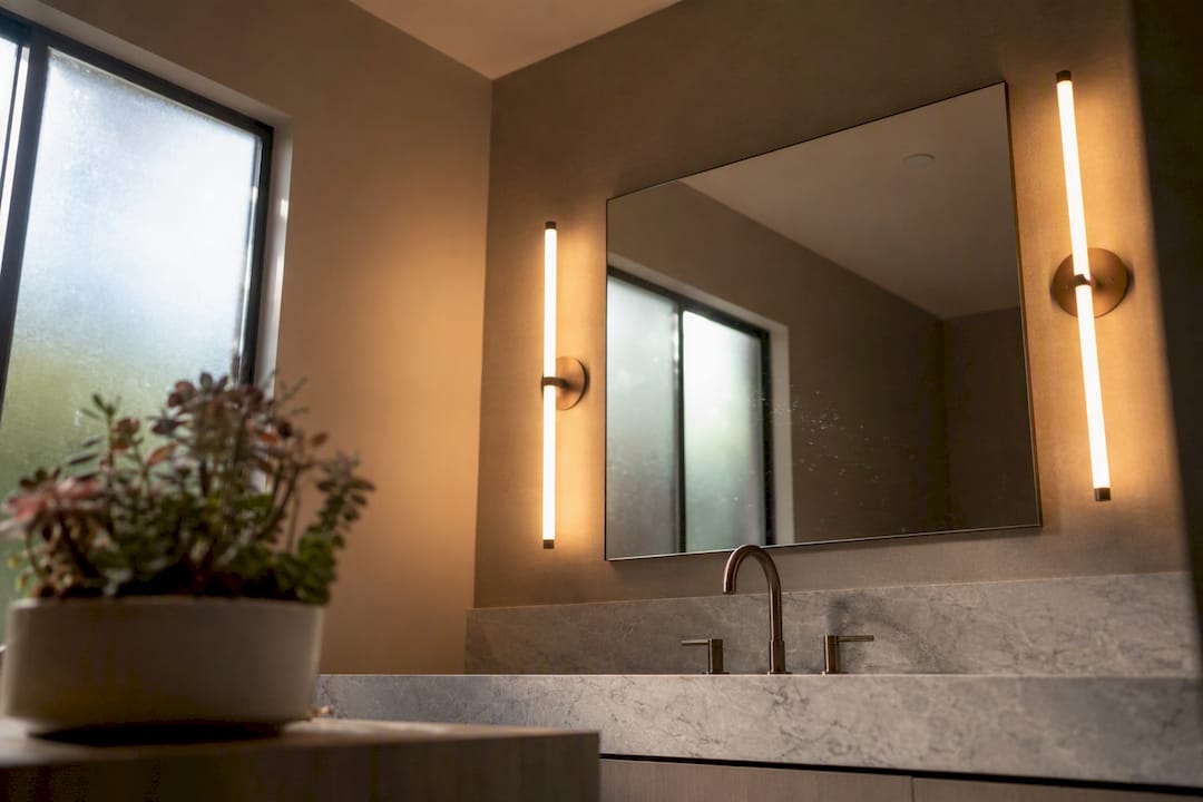 Vertical side sconces lighting a bathroom mirror