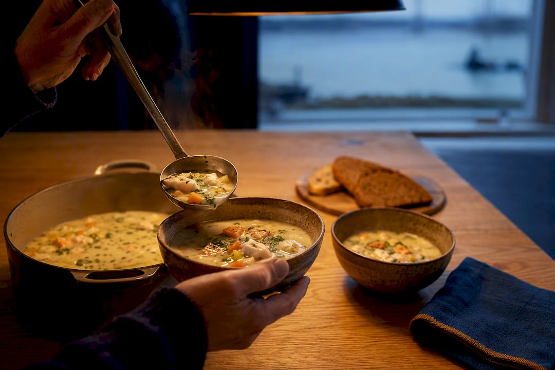 Dampfende Fischsuppe auf einem rustikalen Holztisch