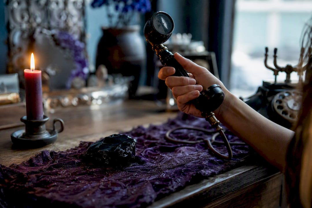 Hand holding phone receiver near candle and crystal