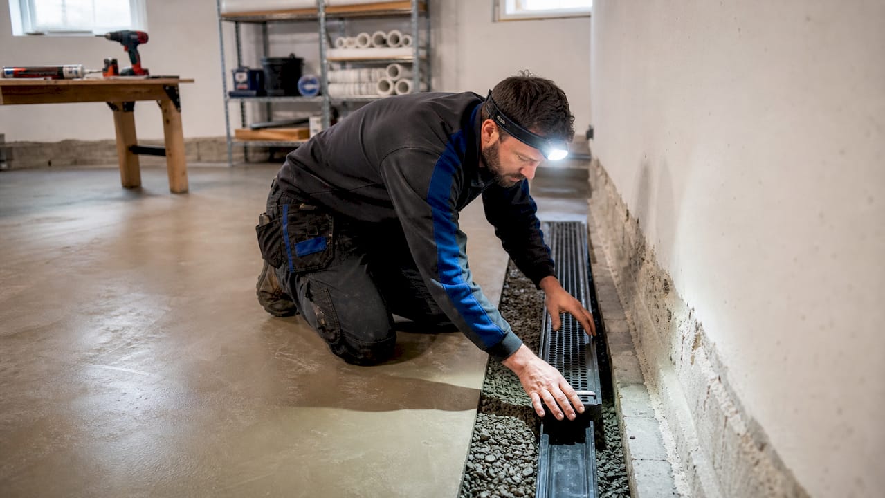 Technician installing interior French drain in basement