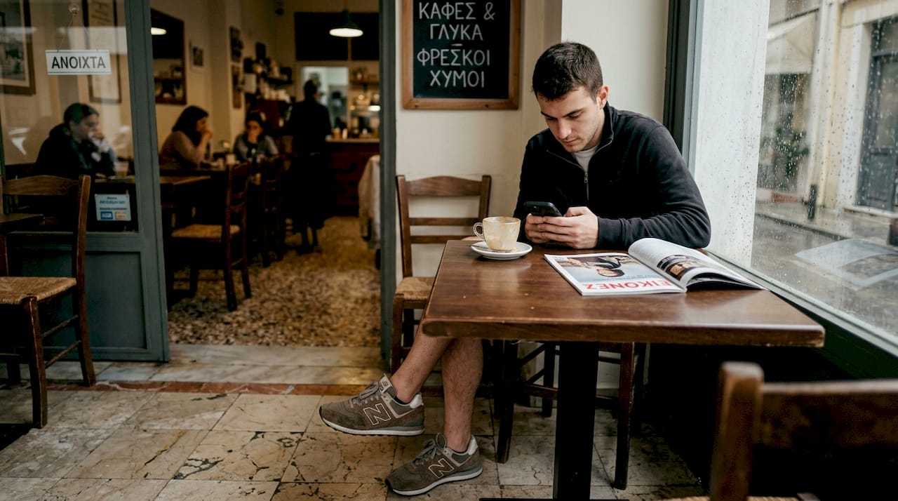 Ένας άνδρας με σουέτ αθλητικά παπούτσια απολαμβάνει το βιβλίο του σε ένα καφέ.