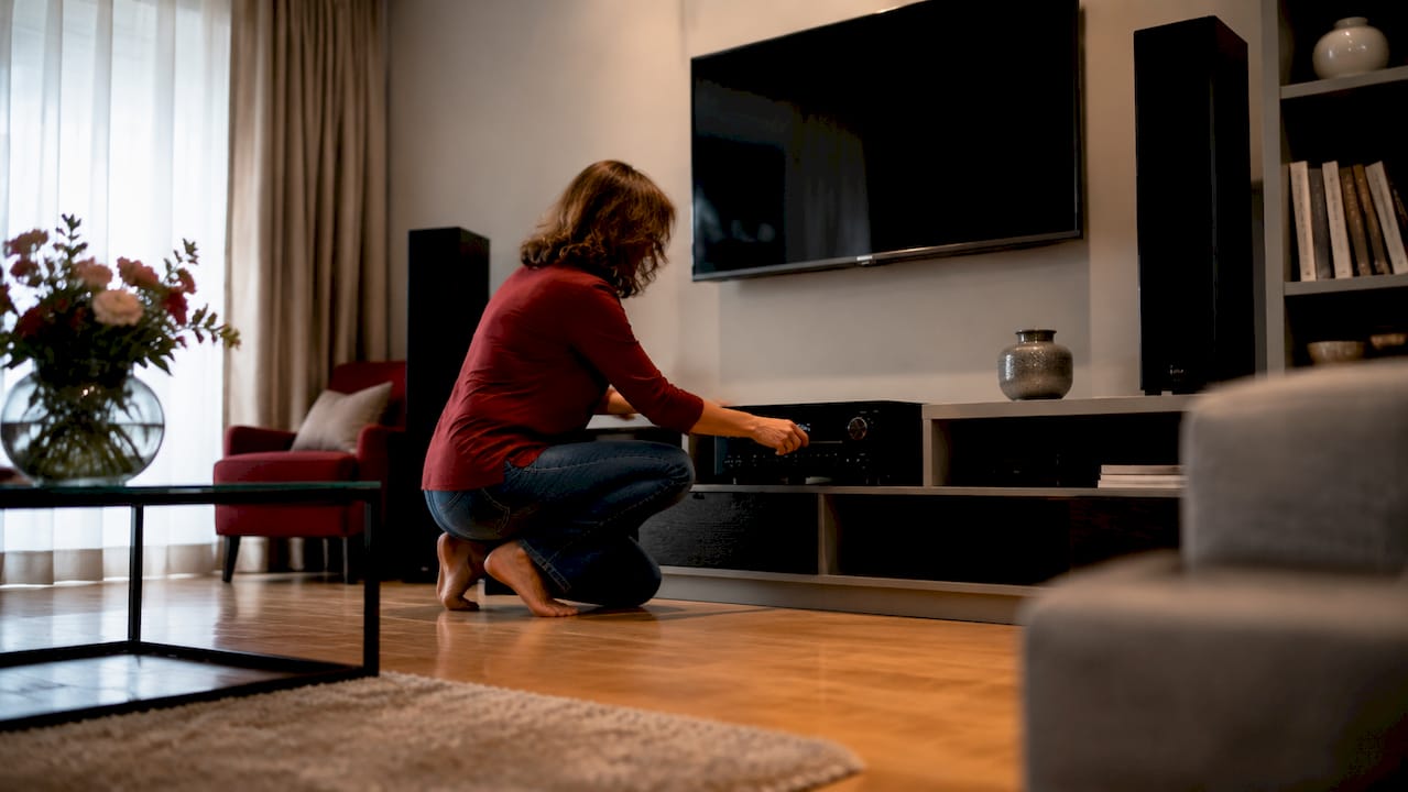Μια γυναίκα ρυθμίζει το soundbar στο σαλόνι της, φροντίζοντας να απολαύσει τον ήχο της αγαπημένης της ταινίας όπως ακριβώς θέλει.