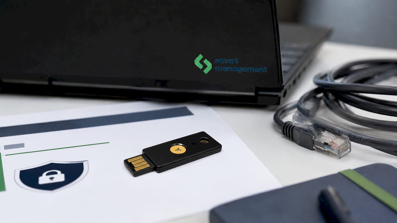 Yubikey ключ за сигурност, поставен на бюро сред различни технологични аксесоари – изглед отгоре.