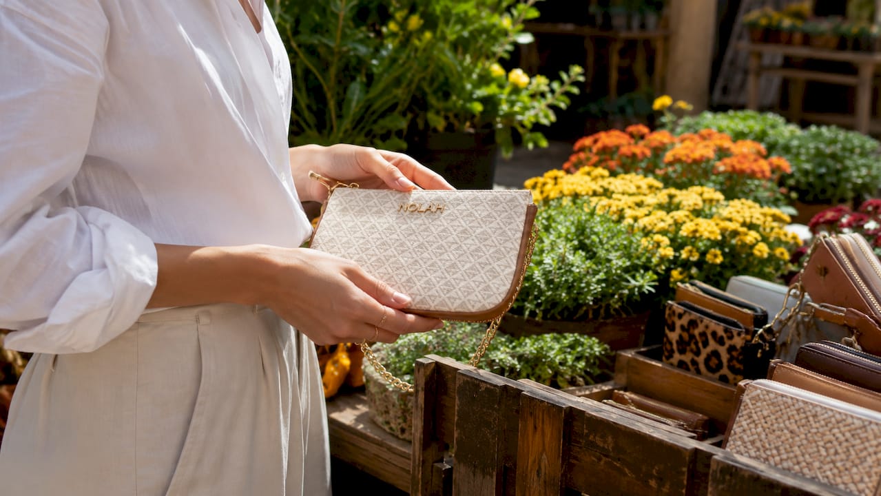 Χέρια κρατούν με χάρη το Nolah clutch πάνω στο μπράτσο του καναπέ, προσθέτοντας στυλ στη στιγμή.