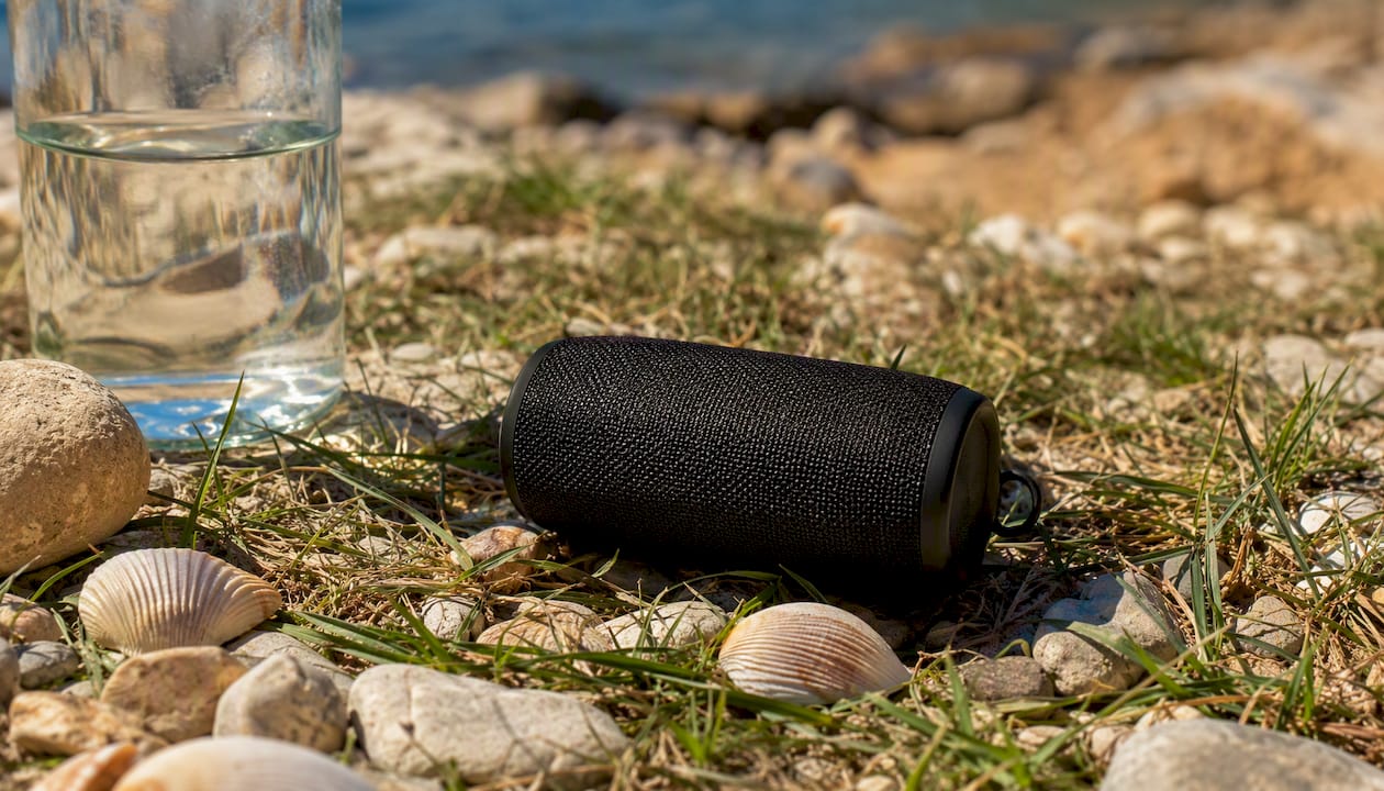 Ένα φορητό ηχείο Bluetooth πάνω σε κουβέρτα πικνίκ, έτοιμο να γεμίσει την ατμόσφαιρα με μουσική στην εξοχή.