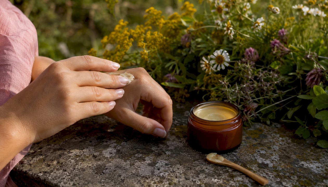 Hands holding beeswax cream jar outdoors