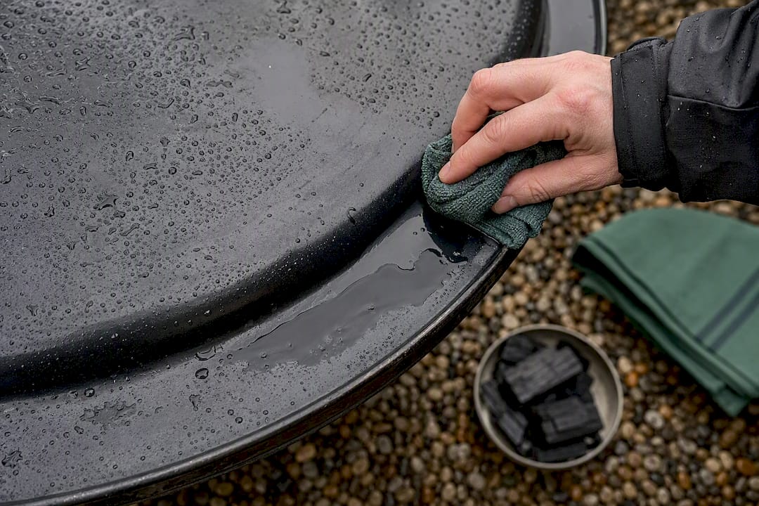 Hand clearing rainwater from barbecue lid
