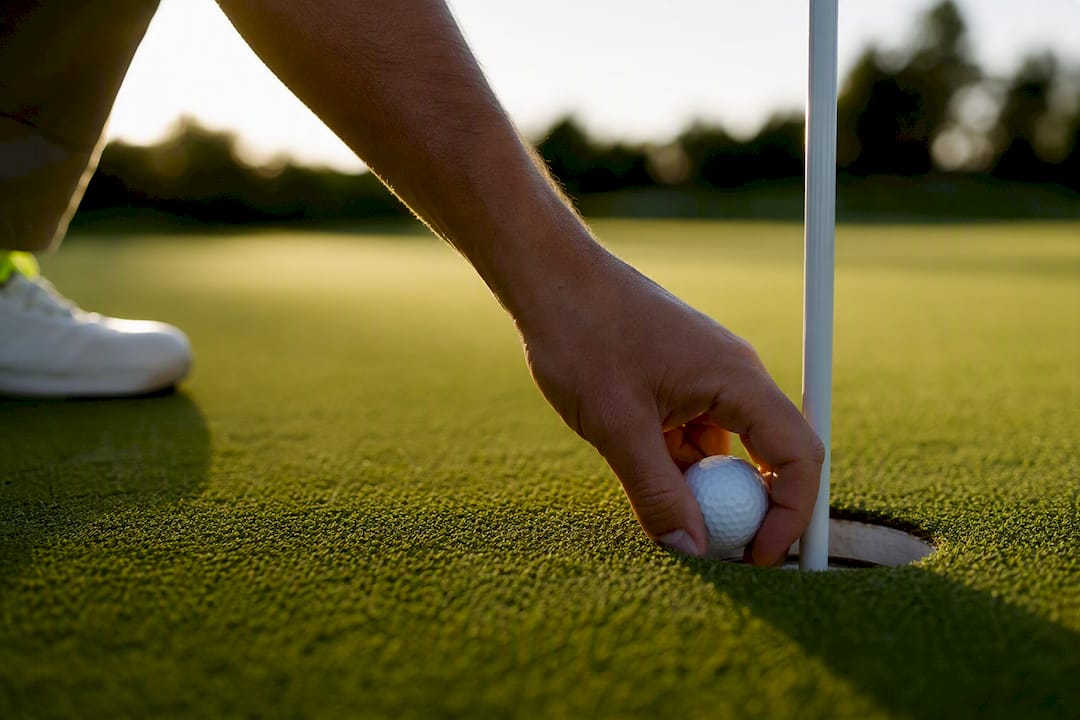 Golfer picking up ball from hole