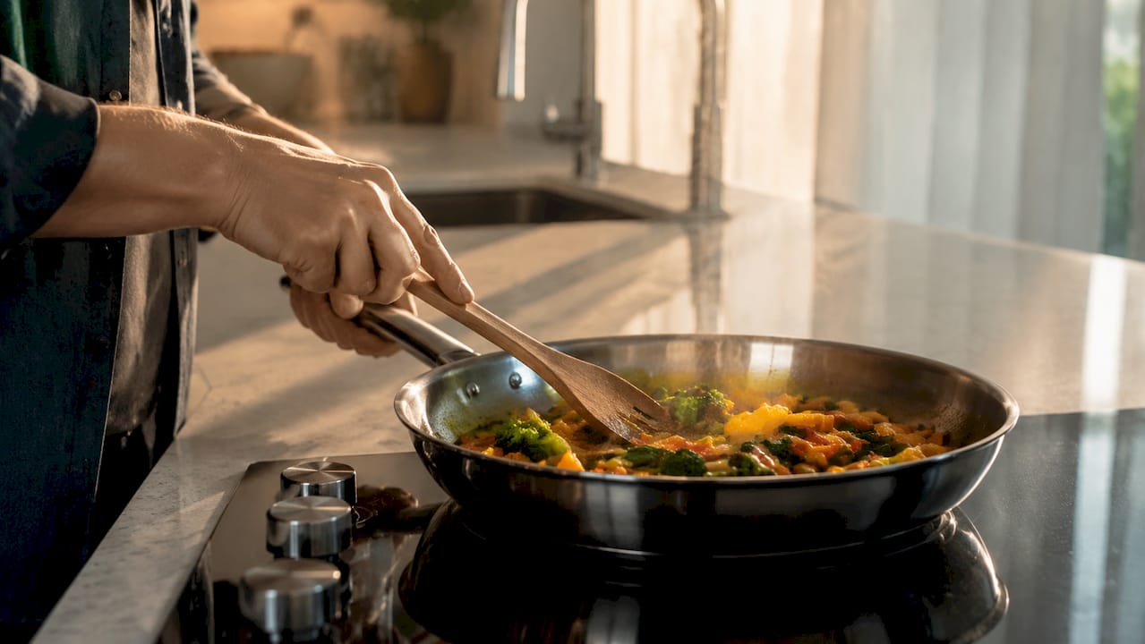 Hands sautéing vegetables in stainless skillet
