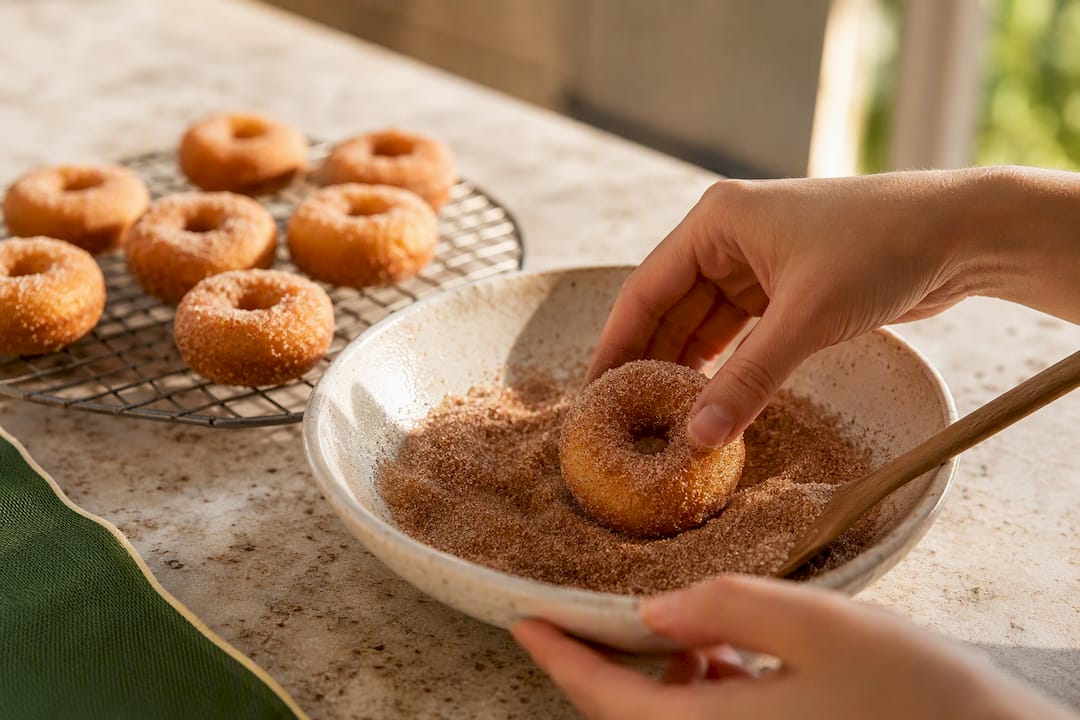 Hands rolling warm mini donuts in cinnamon sugar