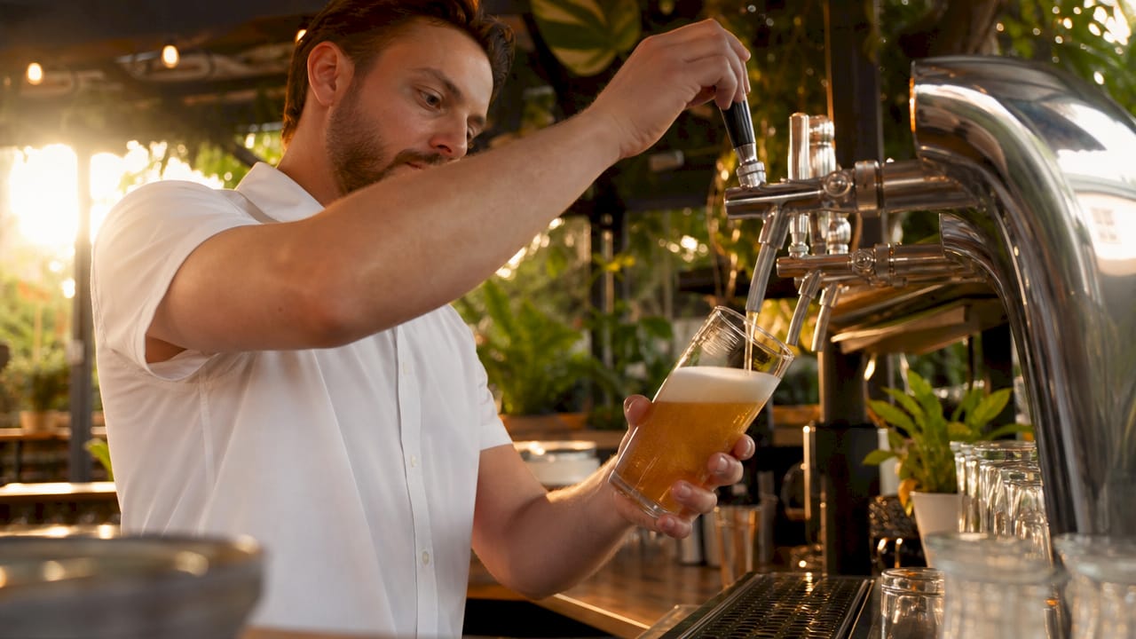 Een barman tapt een vers biertje achter de bar in het café.