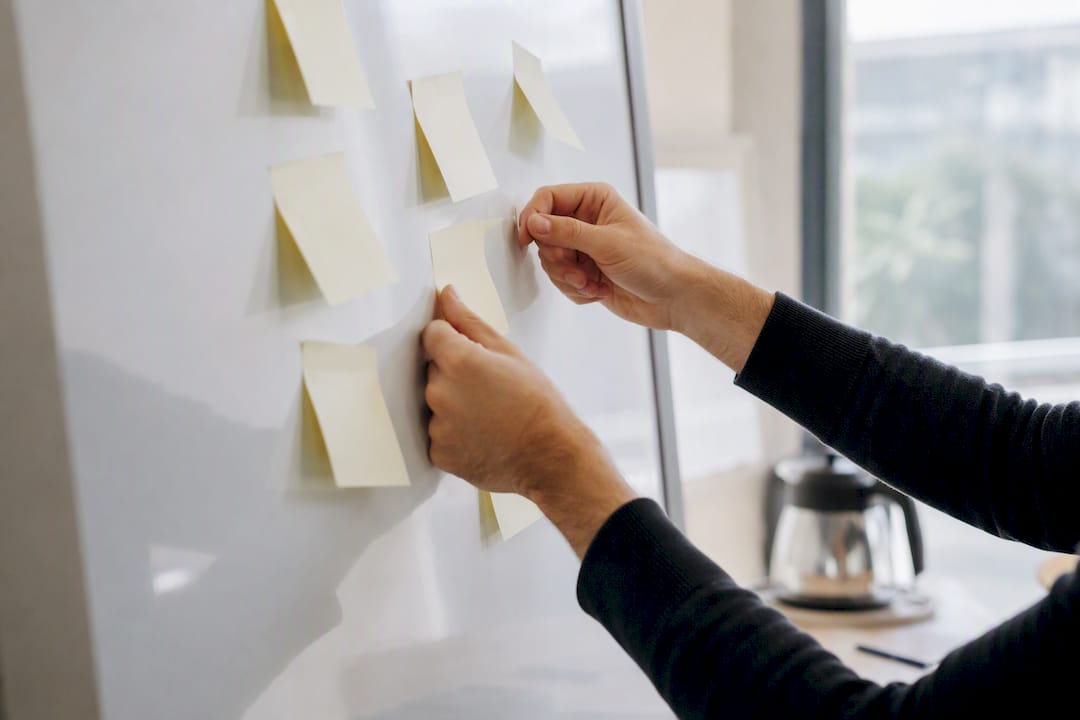 Handen die lege notitieblaadjes op een muur plakken om een strategie uit te stippelen
