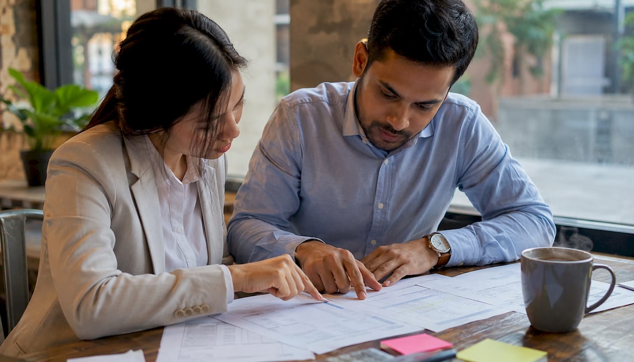 Twee collega’s buigen zich samen over douanedocumenten aan tafel.