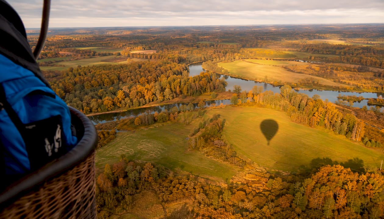 Rudens ainava Latvijā, skatīta no gaisa balona – krāšņi laukumi un meži, kam pāri klājas zelta un sarkanas lapas.