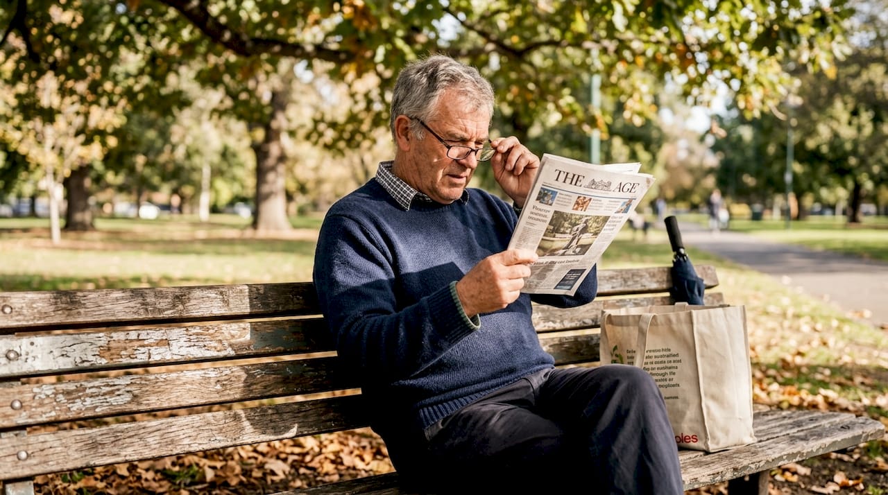 Older man adjusting newspaper with glasses