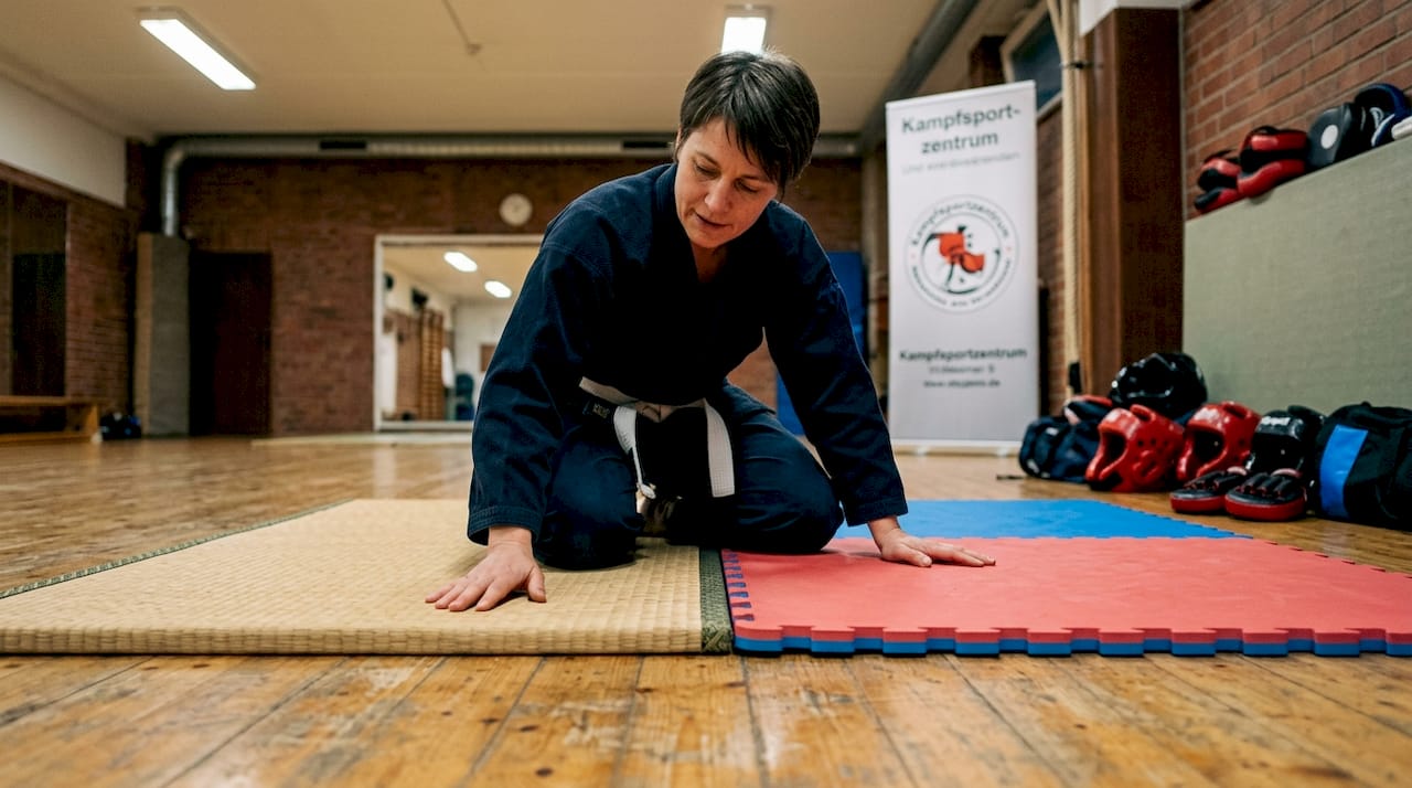 Eine Trainerin nimmt zwei unterschiedliche Tatami-Matten unter die Lupe und zeigt, worin sie sich unterscheiden.
