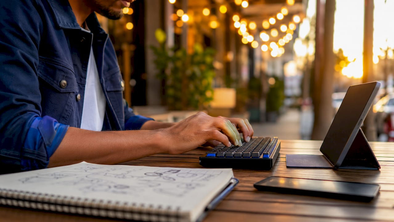 Hands typing on keyboard with tech devices