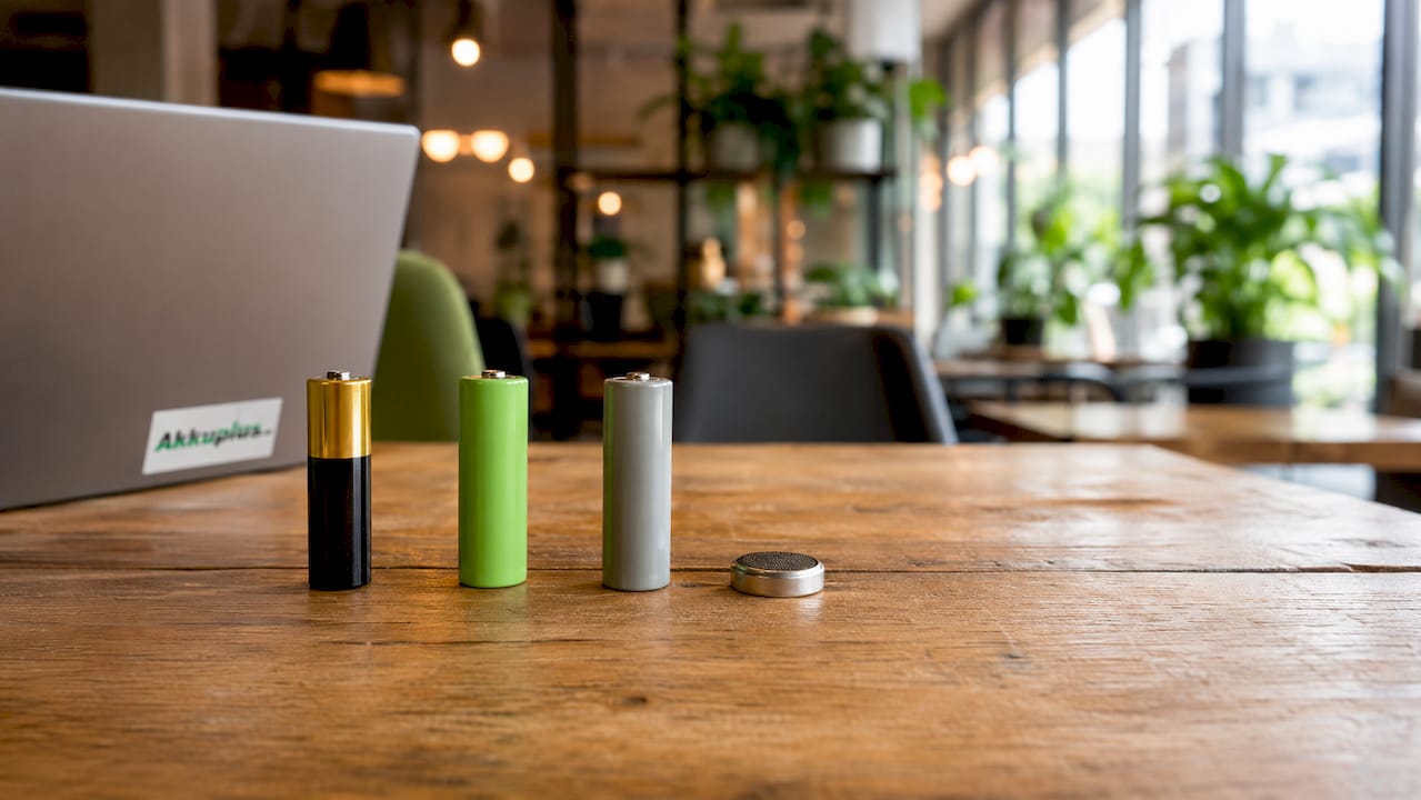 Vier verschiedene Batterien liegen nebeneinander auf einem Holztisch.