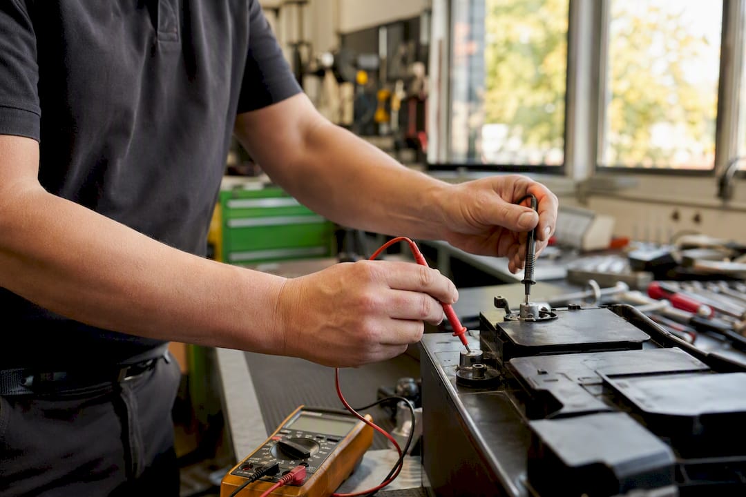 Hände messen die Batteriespannung eines Autos