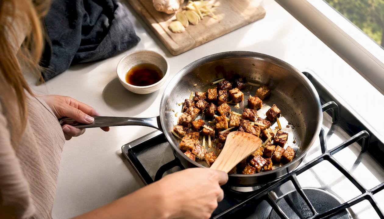 Hands pan-frying tempeh with ginger