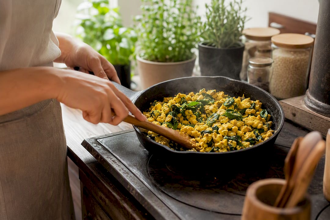 Hands cooking tofu scramble with spinach and turmeric