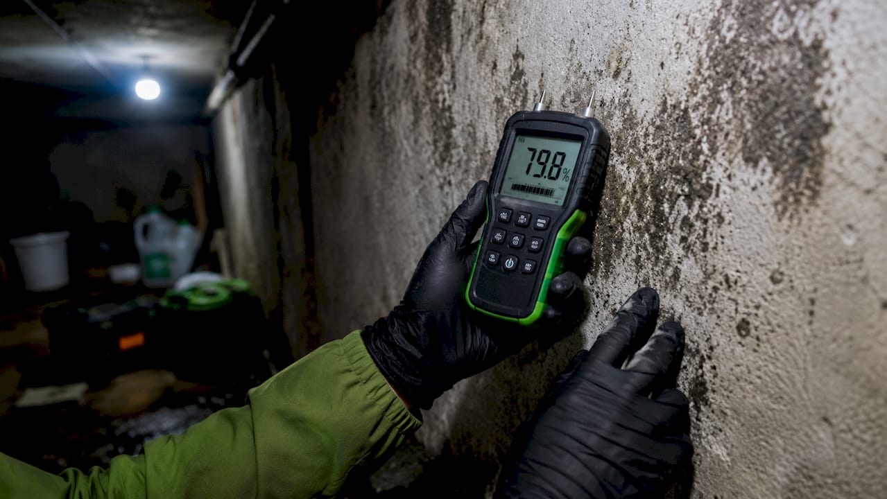 Una persona comprobando la humedad de una pared con un termohigrómetro en mano.