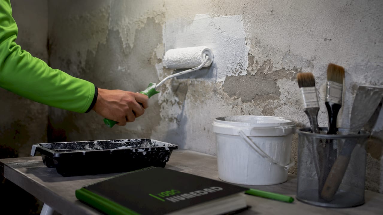 Mano lijando una pared con humedad, al lado de un deshumidificador