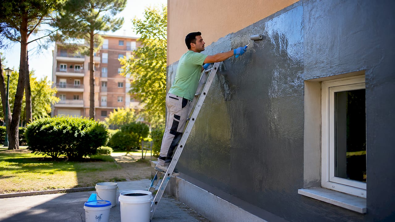 Operario vestido con uniforme celeste trabajando en la impermeabilización de una fachada.
