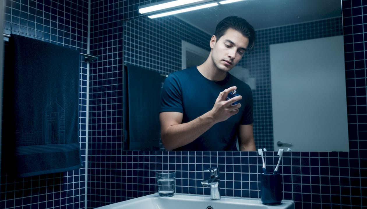 Hombre echándose demasiado perfume en un baño pequeño