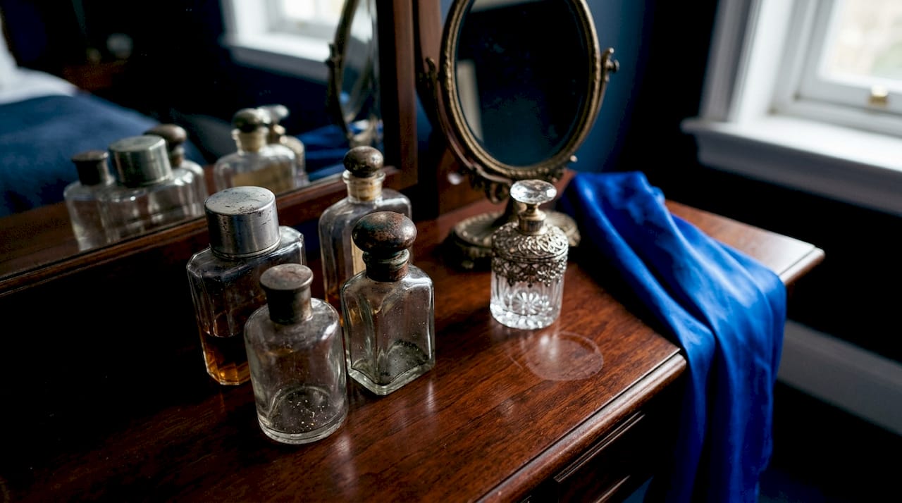 Quelques flacons de parfum rétro soigneusement disposés sur une coiffeuse en marbre, apportant une touche d’élégance intemporelle à la pièce.
