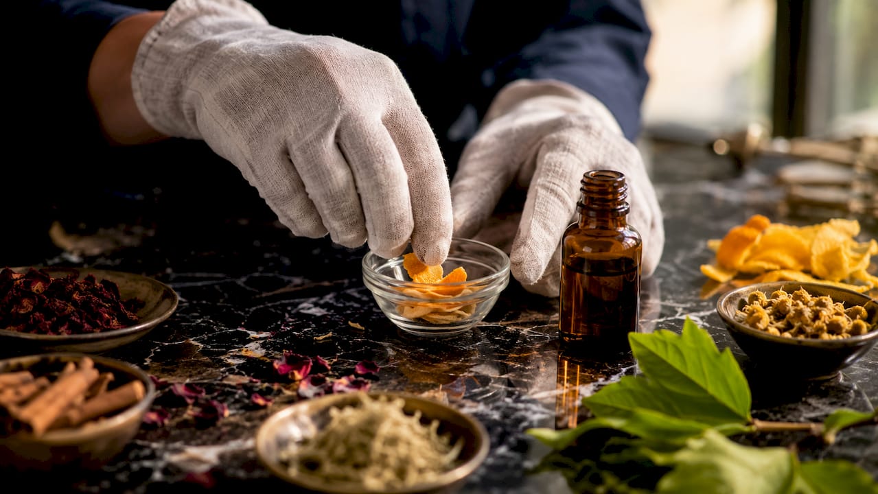Zoom sur des mains en train de disposer avec soin des ingrédients naturels pour créer un parfum.