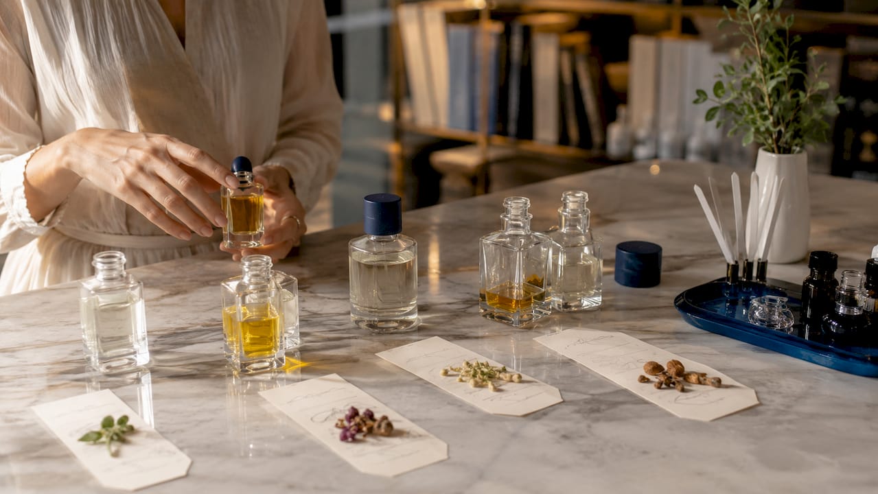 Manos sosteniendo frascos de perfume entre acordes aromáticos
