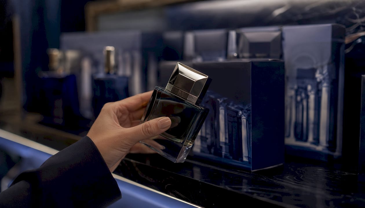 Una mano sostiene un frasco de perfume pesado con tapa metálica.