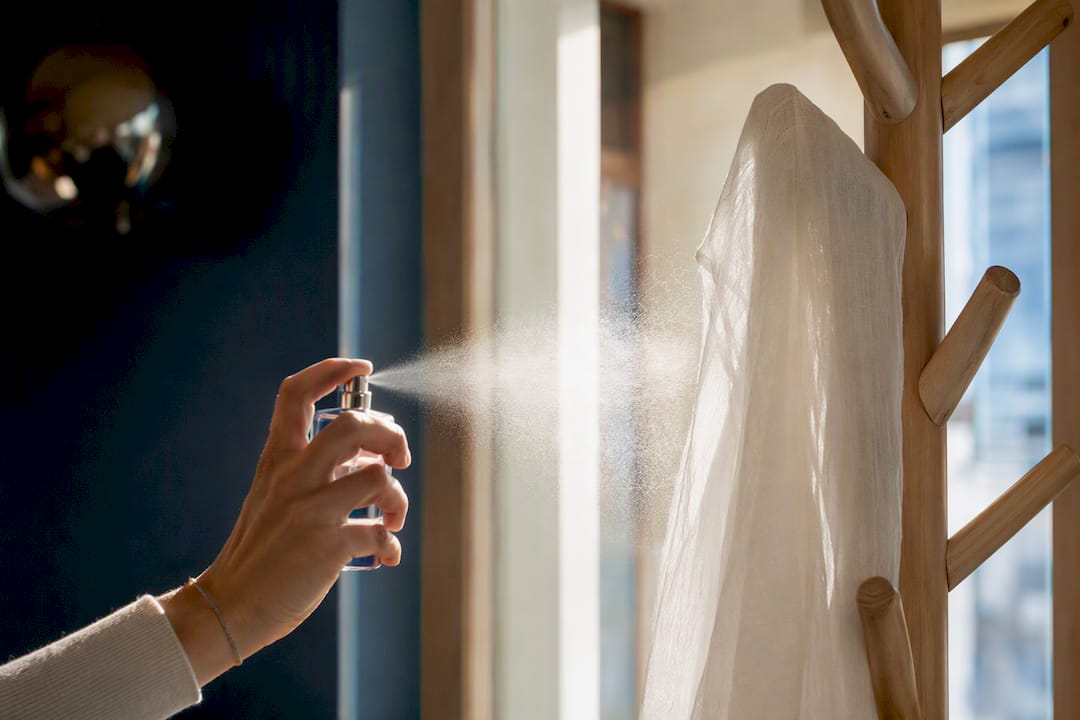 Main vaporisant un parfum aux agrumes sur une écharpe blanche
