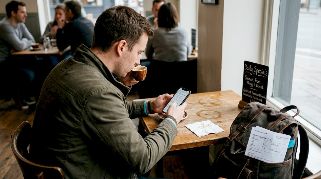 Man booking travel on phone in busy cafe