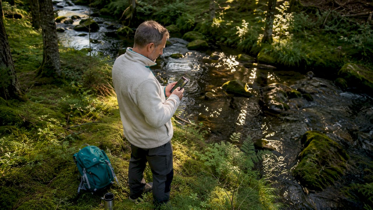 En person står ude i skoven og bruger sin smartphone til at orientere sig og kortlægge området.