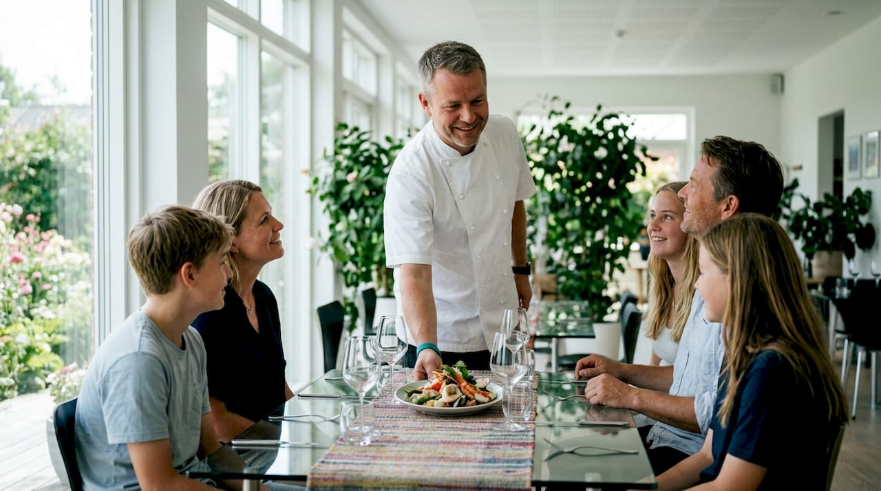 Kokken byder en familie velkommen og serverer deres mad på en hyggelig lokal restaurant.